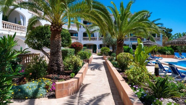 Un resort con zona de piscina, palmeras y un camino que lleva a un edificio con balcones.