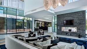 Un salon moderne avec un grand canapé d’angle, une table basse en verre et un téléviseur à écran plat fixé à un mur texturé.