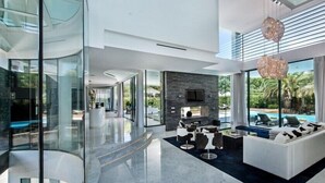 Un salon moderne avec un mur en verre, une cheminée en pierre et une vue sur la piscine.