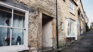 A narrow stone-paved street with traditional stone buildings, one with a visible window and a door leading to a courtyard. - Flints Cottage (Richmond)