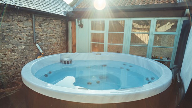 A hot tub in a backyard with stone walls and a wooden door. - Flints Cottage (Richmond)