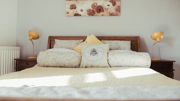 A neatly made bed with a patterned bedspread, two bedside lamps, and a decorative pillow with a bee design.