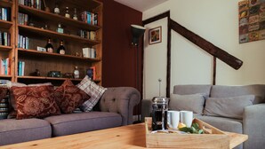 A living room with a sofa, a coffee table, and a bookshelf filled with books and bottles. - Flints Cottage (Richmond)