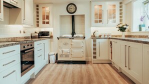 A modern kitchen with white cabinetry, a built-in oven, a microwave, and a clock on the wall. - Flints Cottage (Richmond)