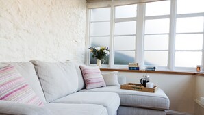 A cozy living room with a light grey sofa, a small side table with a tray of items, and a window with a view of the outdoors. - Flints Cottage (Richmond)