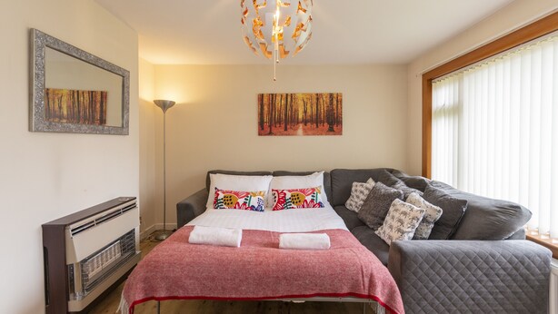 A bedroom with a bed, a grey sofa, a floor lamp, a mirror, and artwork on the walls.