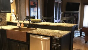 Una cocina con lavavajillas integrado, encimeras de granito, muebles oscuros y suelo de madera.