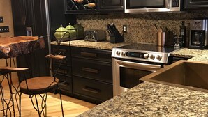 Cocina con armarios oscuros, encimera de granito, microondas de acero inoxidable, estufa a gas y una estantería para vinos.