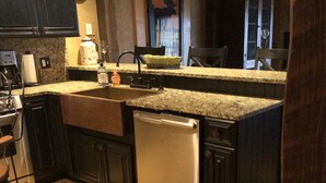 Una cocina con armarios oscuros, lavavajillas de acero inoxidable, encimera de granito y suelo de madera.