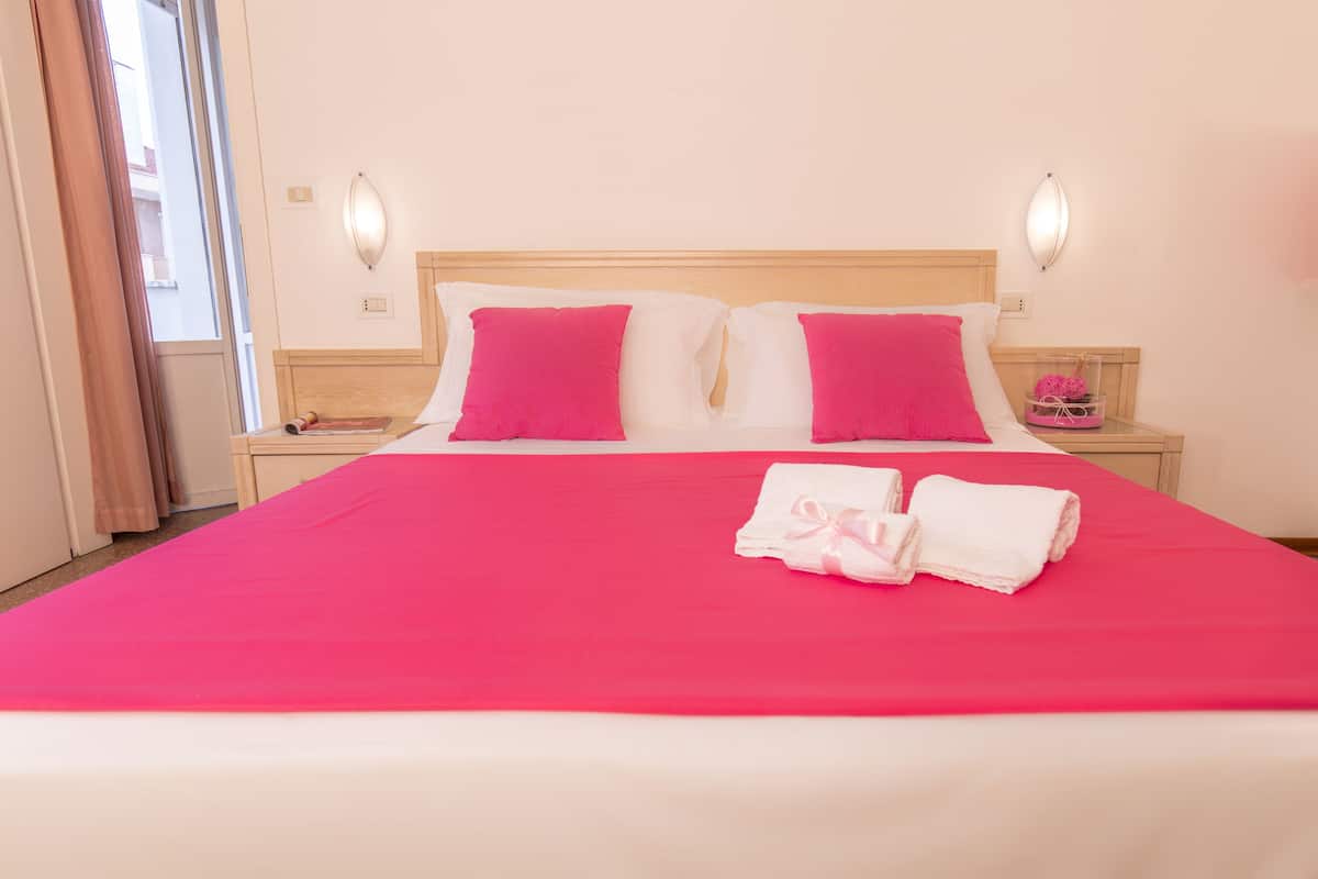 Une chambre d’hôtel avec un grand lit, deux oreillers, une table de chevet avec une lampe et une fenêtre avec des rideaux.