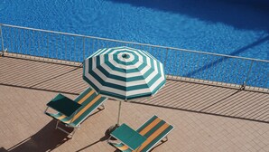 A poolside area with a tiled deck, a striped umbrella, and two lounge chairs. - Hotel Villa Sole (Bellaria-Igea Marina)