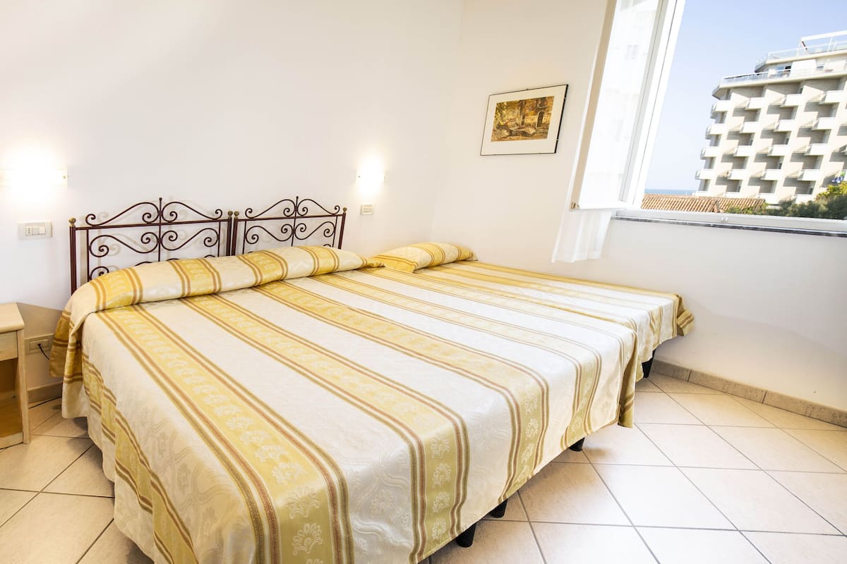 Une chambre d’hôtel avec un lit, une table de chevet, une fenêtre donnant sur la ville et un tableau encadré au mur.