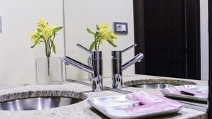 A bathroom with a granite countertop, a sink, a mirror, and a vase with yellow flowers. - Hotel Villa Sole (Bellaria-Igea Marina)