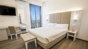 A modern hotel room with a large bed, a desk with a chair, a TV mounted on the wall, and a balcony with a view of the sea. - Hotel Villa Sole (Bellaria-Igea Marina)