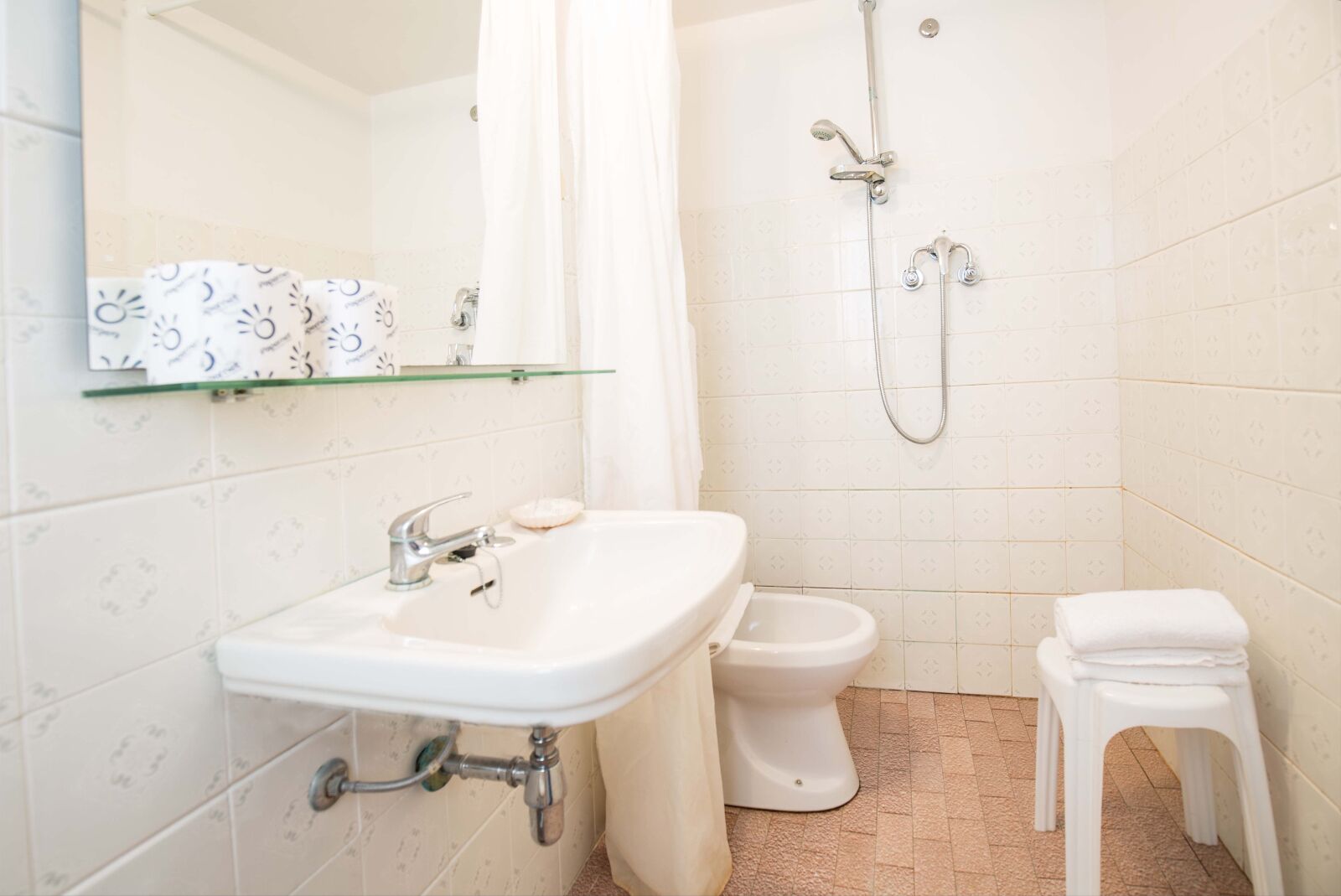 A bathroom with a sink, toilet, shower, and a small stool.