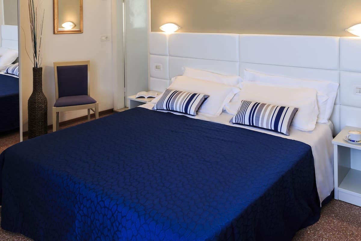 Une chambre d’hôtel avec un grand lit, deux tables de chevet, une chaise et un miroir.