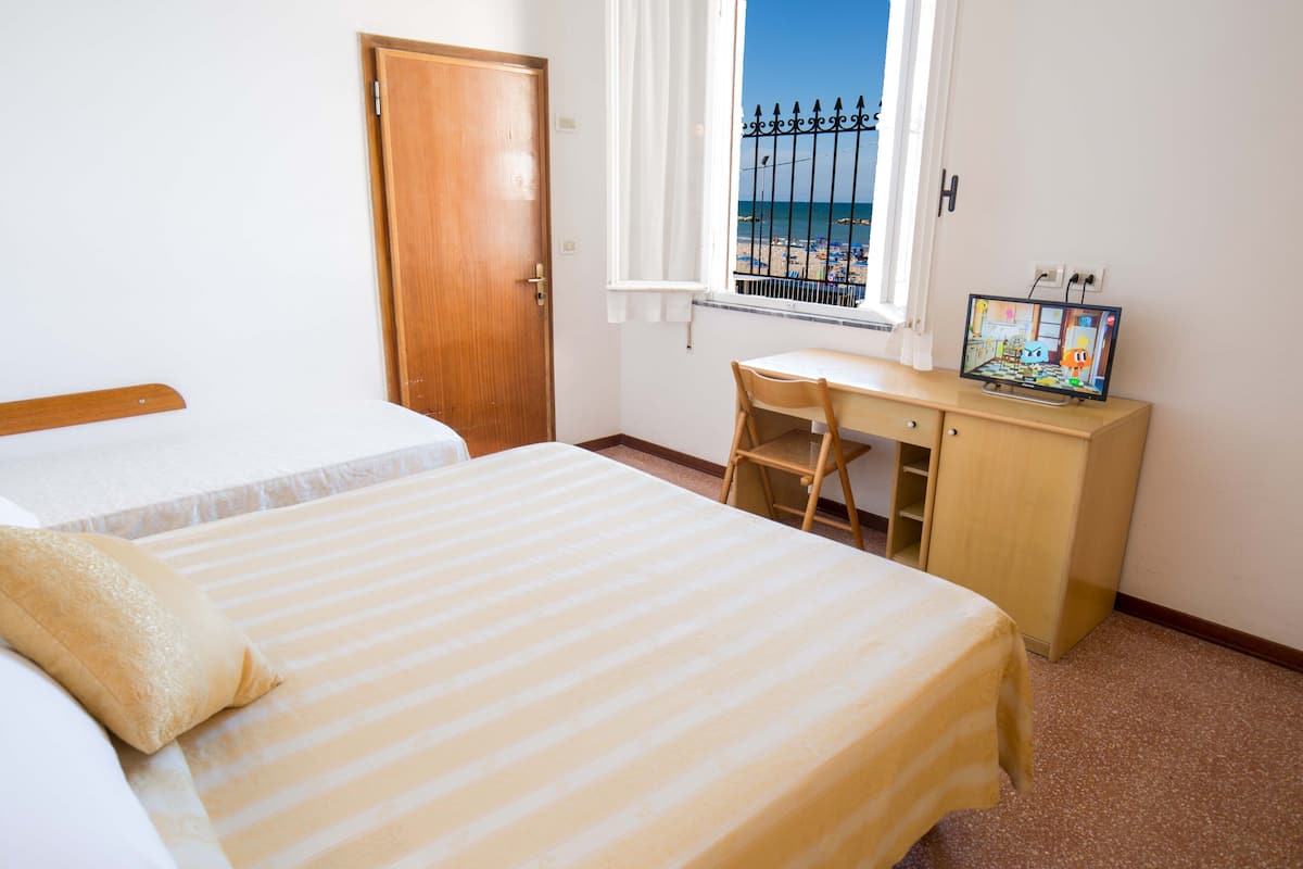 Une chambre avec deux lits, un bureau et une fenêtre donnant sur la plage.