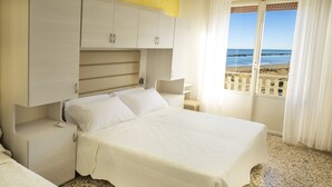 A bedroom with a bed, nightstands, a wardrobe, and a view of the beach. - Hotel Villa Sole (Bellaria-Igea Marina)