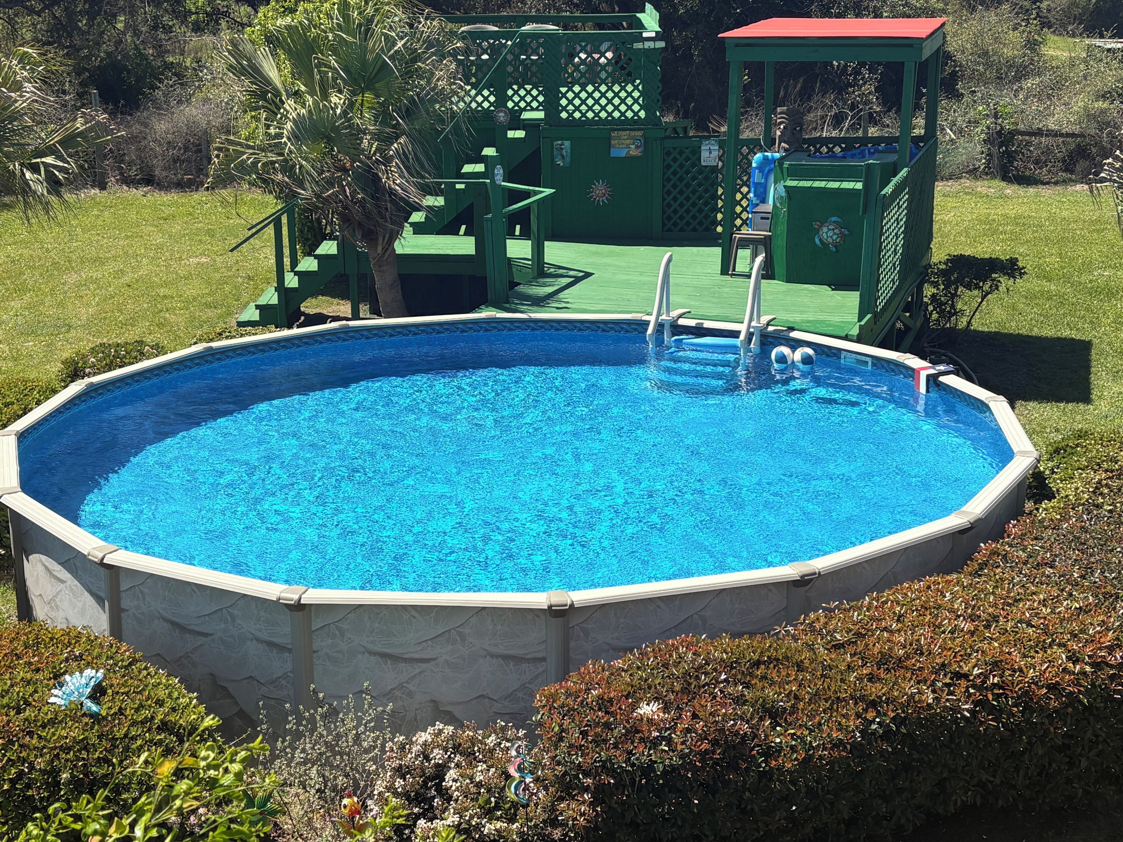 An above-ground swimming pool with a ladder, surrounded by a green deck and a small gazebo.