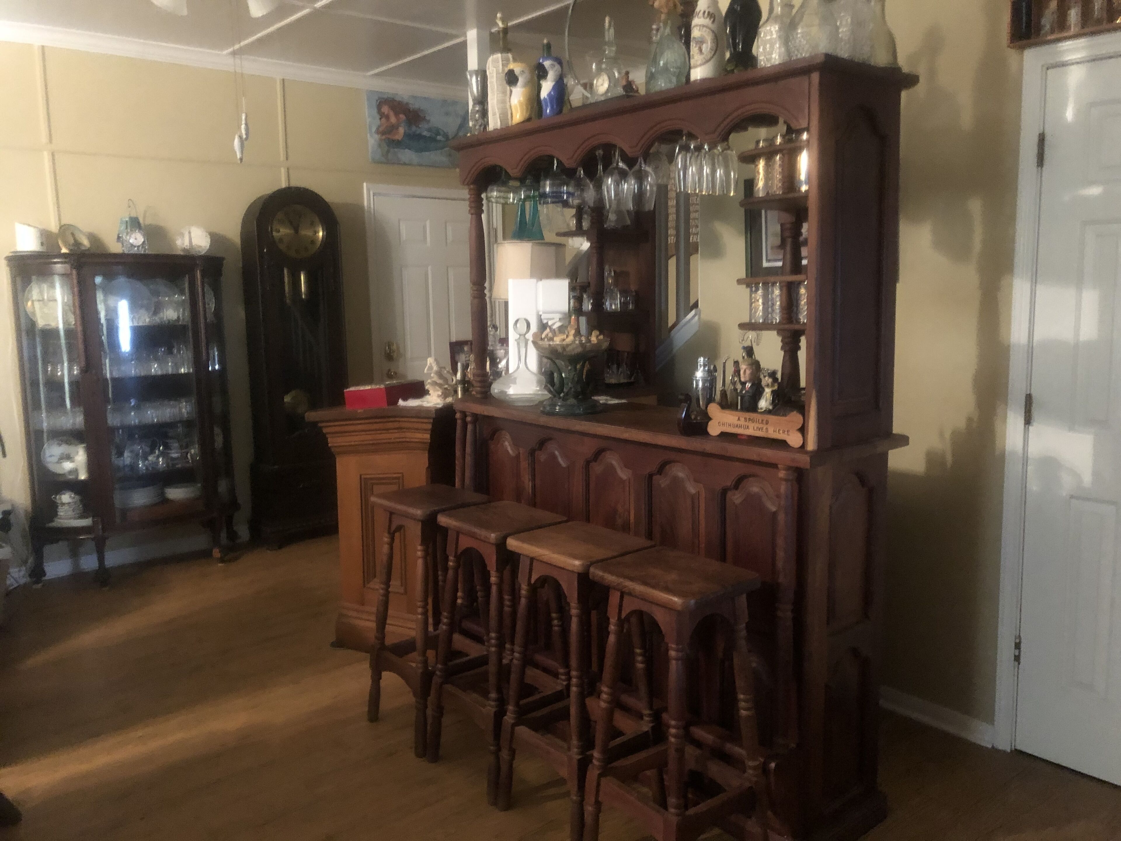 A bar area with wooden stools, a bar counter, and shelves with glassware and bottles.
