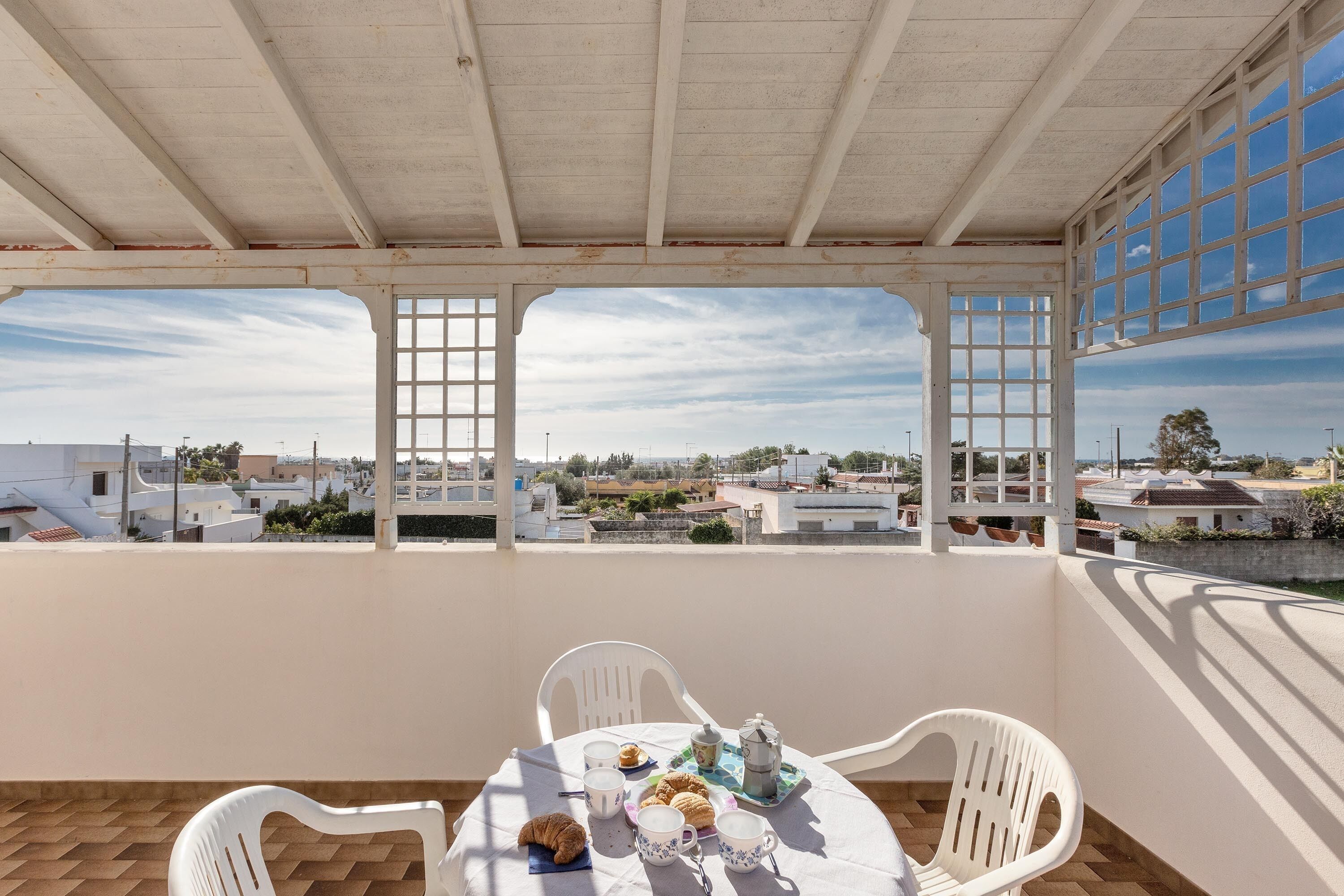 A balcony with a table set for breakfast, white chairs, and a view of the cityscape.