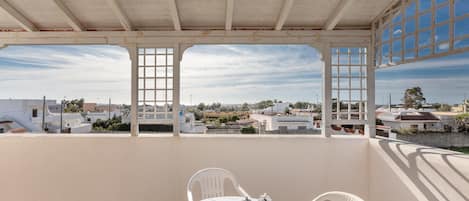 A balcony with a table set for breakfast, white chairs, and a view of the cityscape.