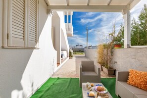A covered outdoor area with wicker furniture, a dining table with food, and a view of a building in the background.