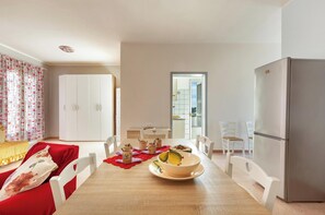 A modern living room with a dining area, white furniture, and a large window.