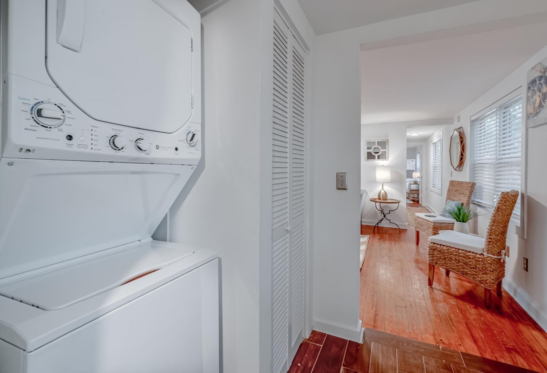 A laundry area with a washing machine and dryer, a hallway leading to a dining area with a table and chairs, and a window with blinds.