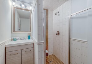 A bathroom with a white vanity, a large mirror, a shower with a glass door, and a tiled floor. - Charming 1950s Beach Cottage Apt B (Isle of Palms)