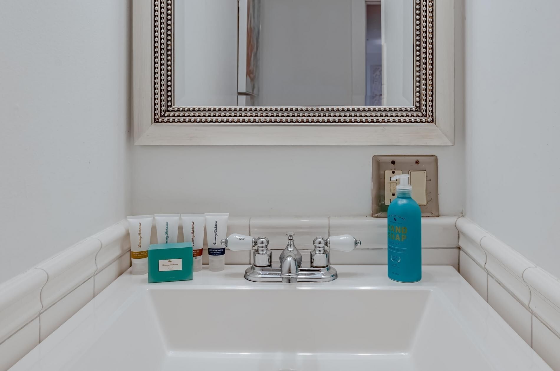 Un lavamanos de baño con artículos de aseo, un espejo y un interruptor de luz.