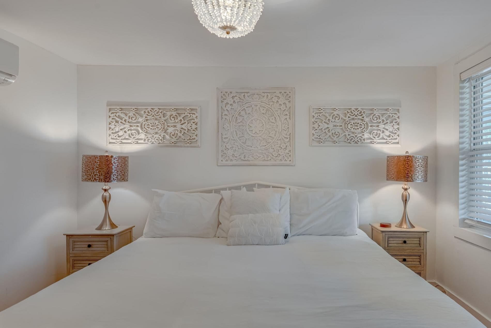 A bedroom with a large bed, two nightstands, decorative wall panels, and a chandelier.