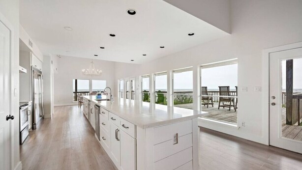 A spacious kitchen with a large island, wooden flooring, and a view of the ocean through large windows. - Beachfront Beauty with Huge Deck & Stunning Views (Galveston)