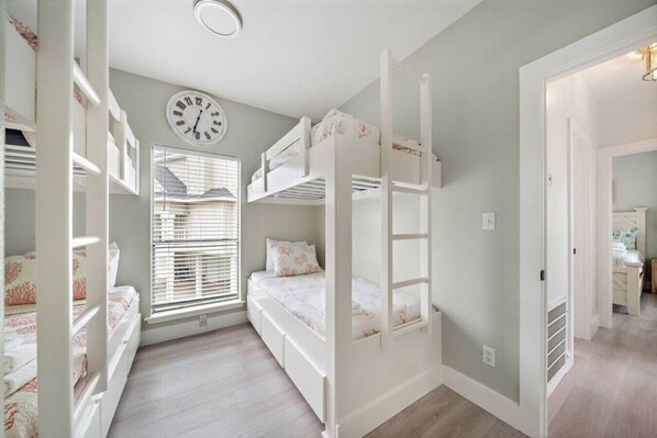 A children's bedroom with bunk beds, a clock, and a window with blinds.