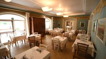 Una sala da pranzo con diversi tavoli e sedie, ampie finestre e una porta in legno.