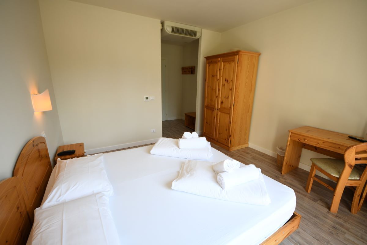 A hotel room with a large bed, a wooden desk, a chair, and a wardrobe.