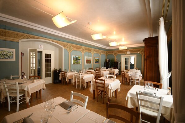 Un comedor con varias mesas dispuestas para recibir a los comensales, con un diseño clásico que incluye candelabros y una pared azul.