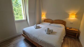Ein Schlafzimmer mit einem hölzernen Bett, weißen Leinen, zwei Nachttischlampen, einem Nachttisch und einem Fenster mit Vorhängen.