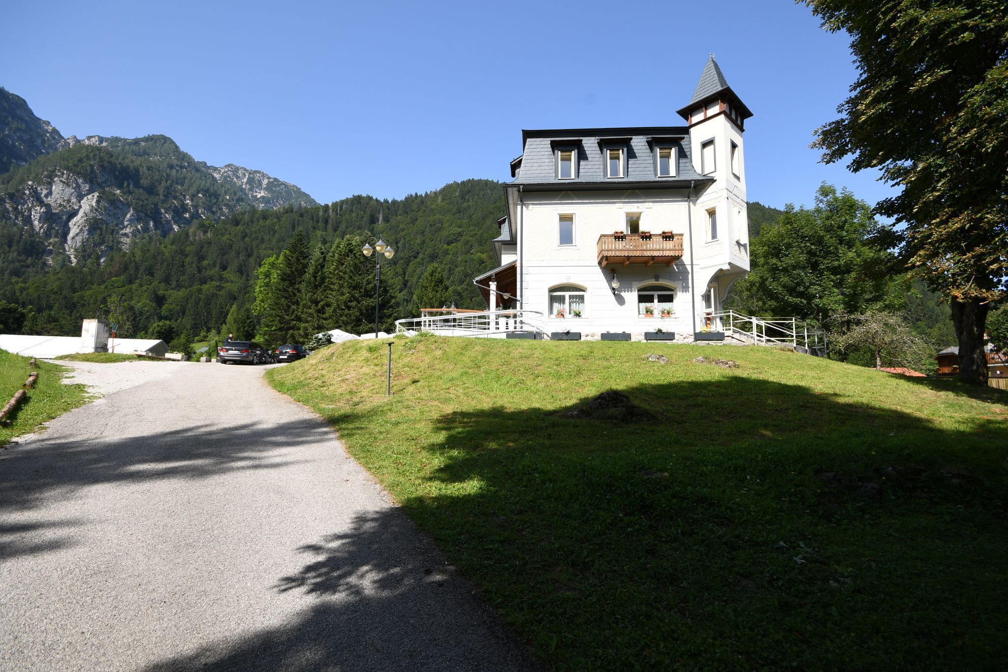 A large, white building with a tower, surrounded by a grassy area and mountains in the background.