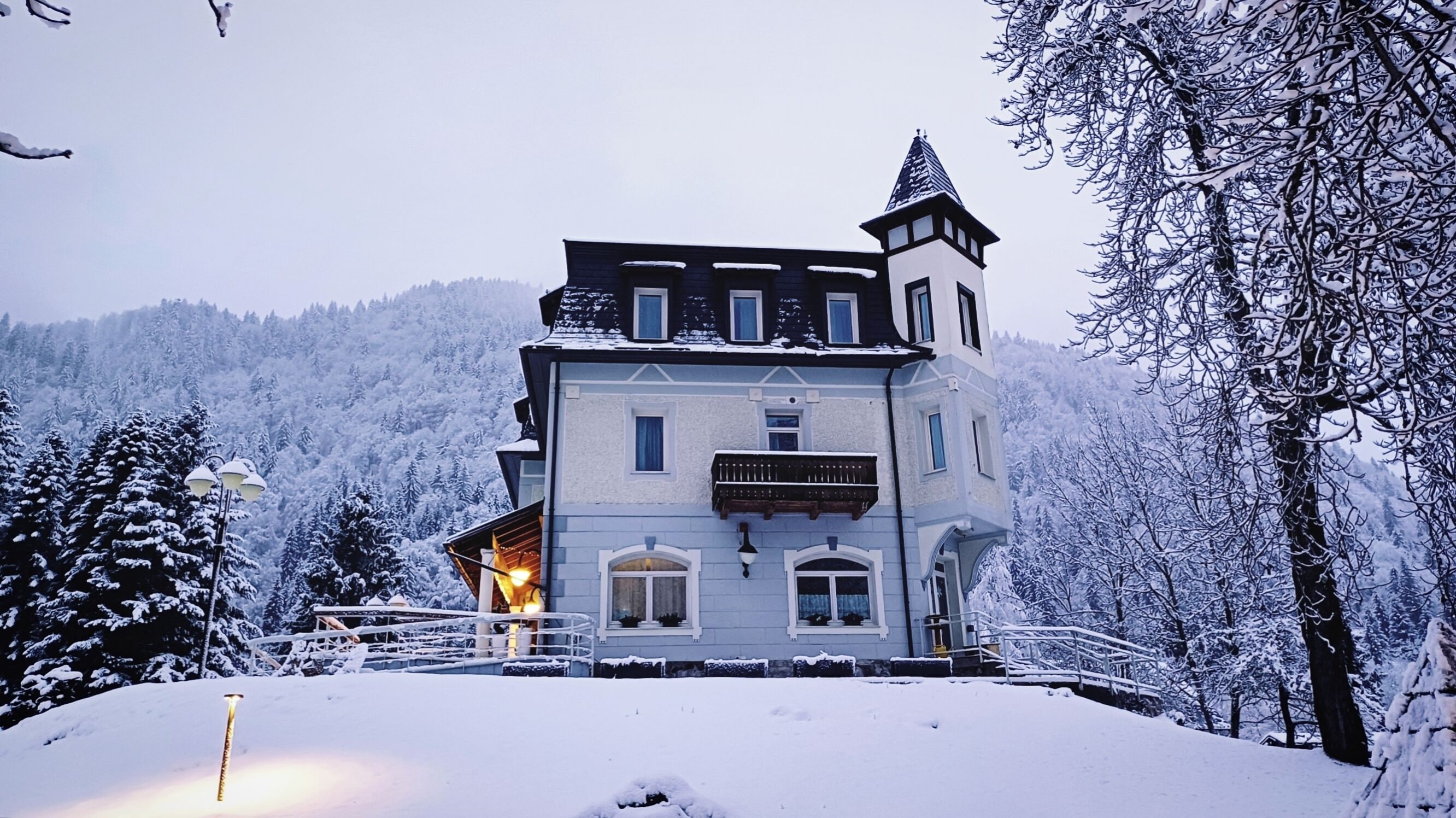 Een gebouw bedekt met sneeuw, met een balkon en een toren, omgeven door sneeuwzware bomen.