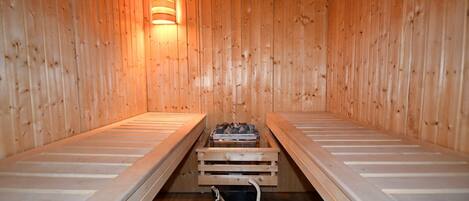 Uma sauna com bancos de madeira e um banco no centro, e um balde no chão.