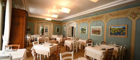 Un comedor con varias mesas dispuestas para el servicio, un armario de madera y cuadros en las paredes.