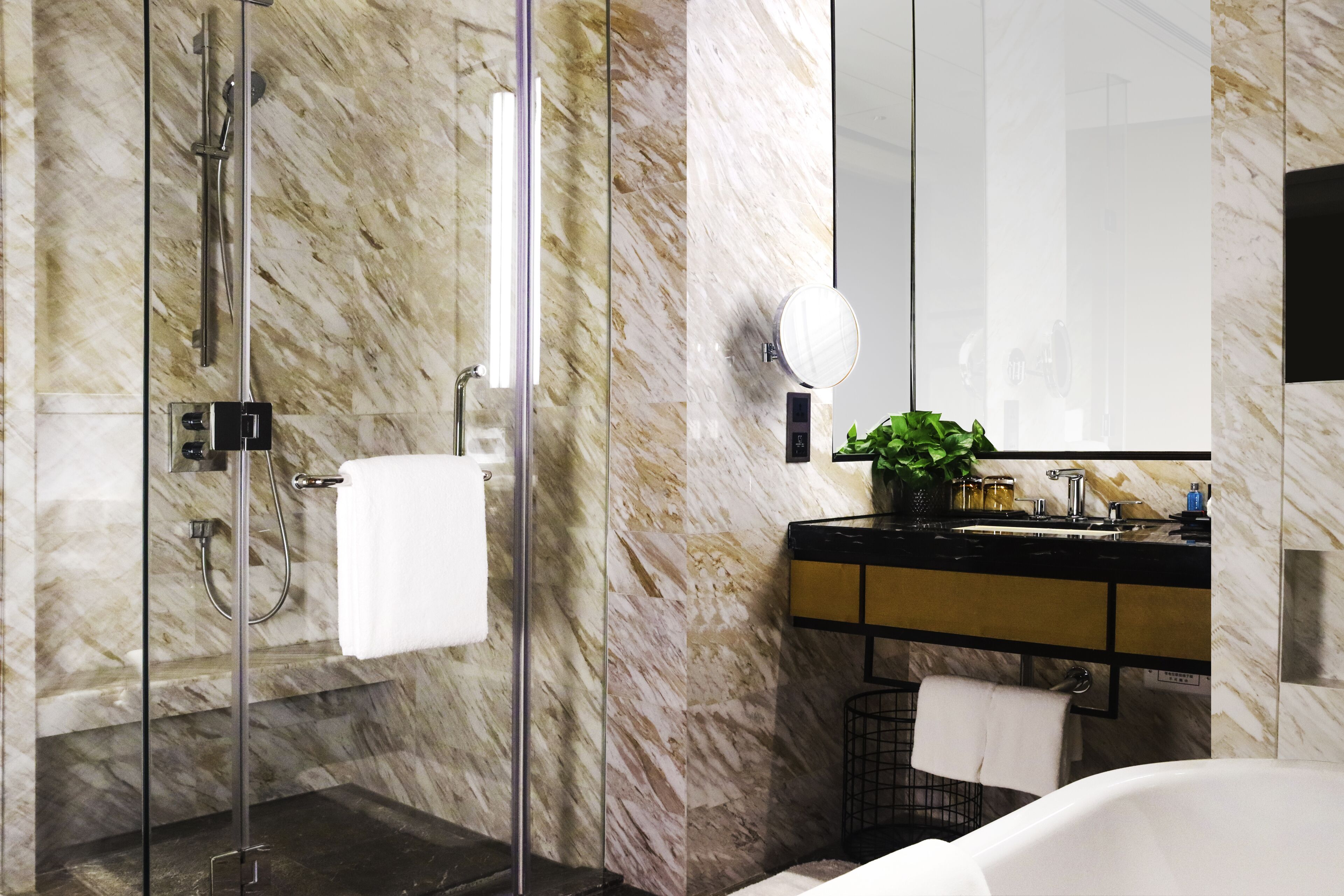 Une salle de bain moderne avec une douche en verre, un mur en marbre, un lavabo avec un miroir et une baignoire blanche.