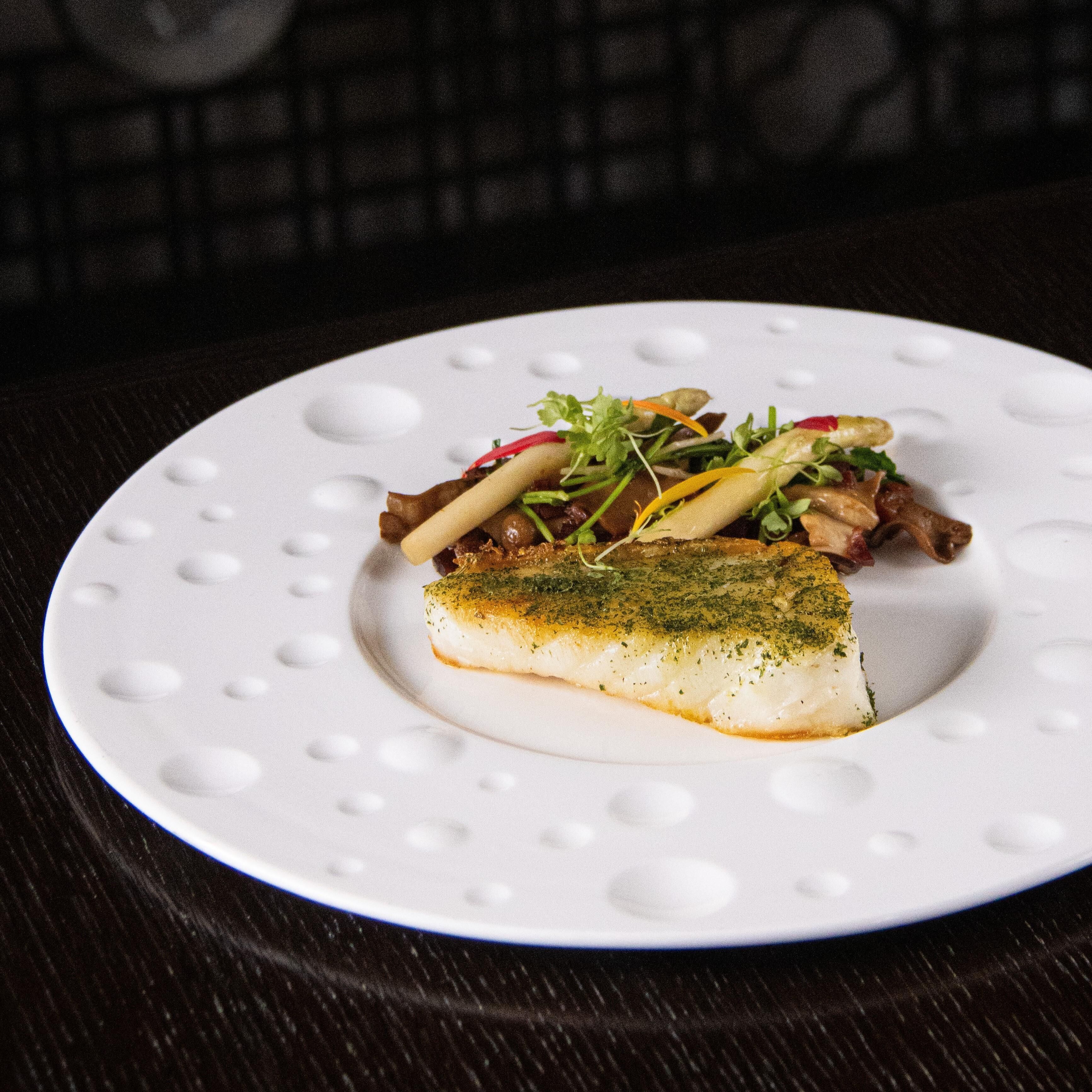 Une assiette blanche avec un morceau de poisson et une salade, posée sur une table en bois foncé.