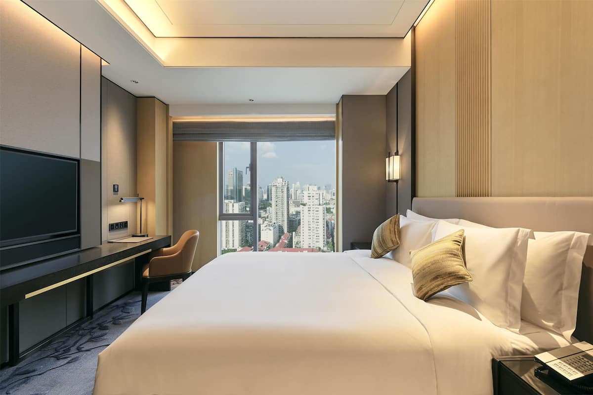 Quarto de hotel com uma cama grande, uma escrivaninha, uma cadeira, uma televisão e vista para a cidade.