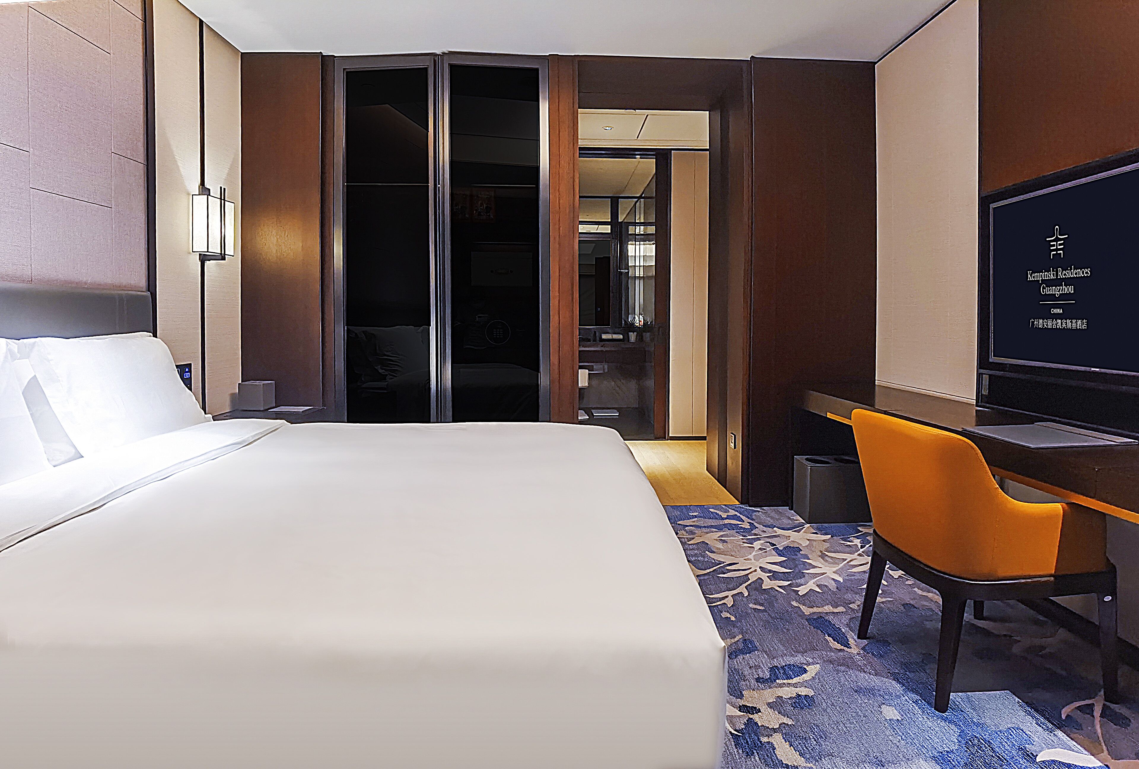 Une chambre d’hôtel avec un grand lit, un bureau, une chaise orange et un téléviseur.