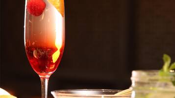 A glass of red beverage with fruit garnish, a bowl of soup, and a jar of pickles on a table.