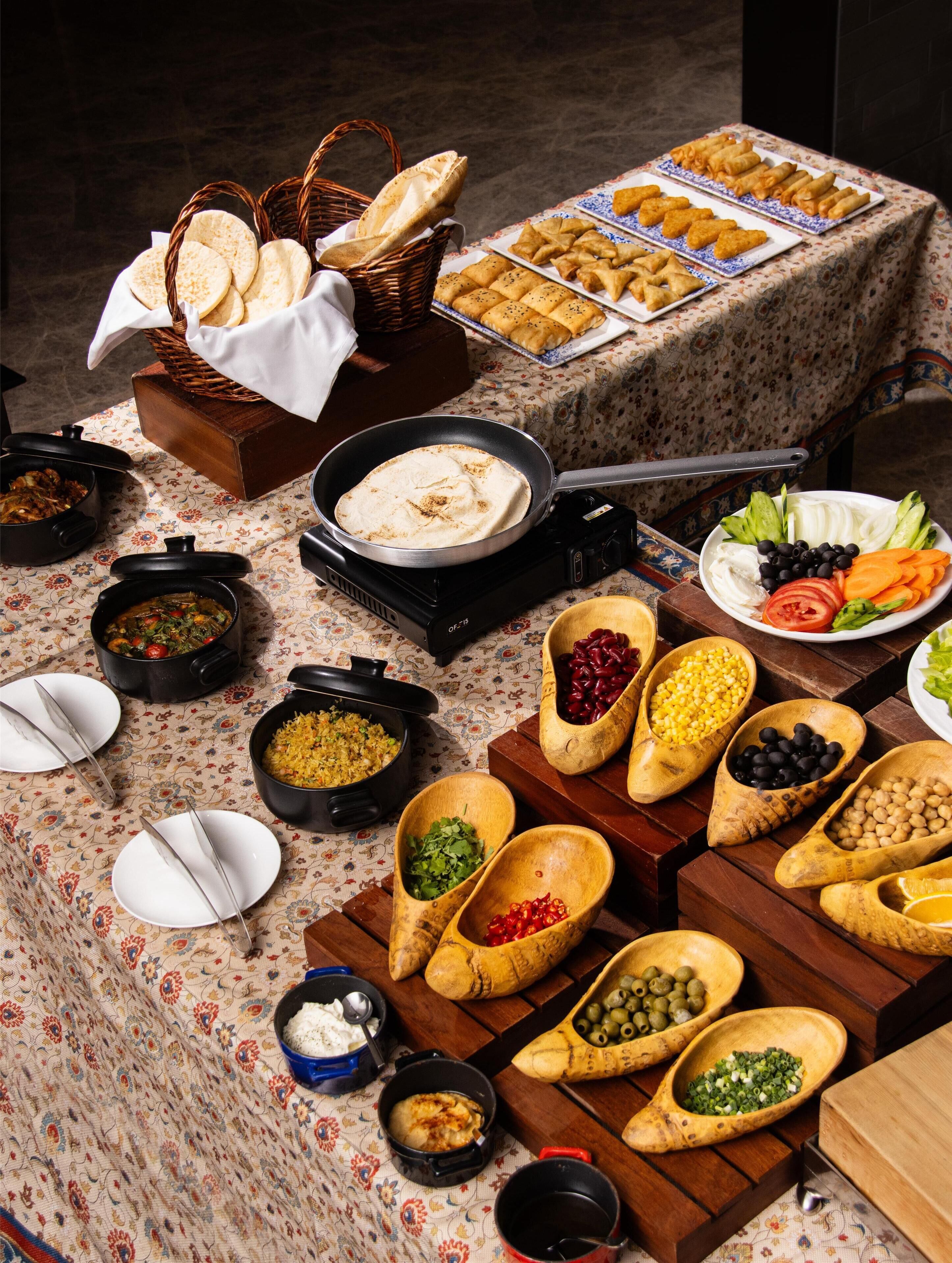 A buffet table with various dishes, including flatbreads, samosas, and a variety of dips and side dishes.