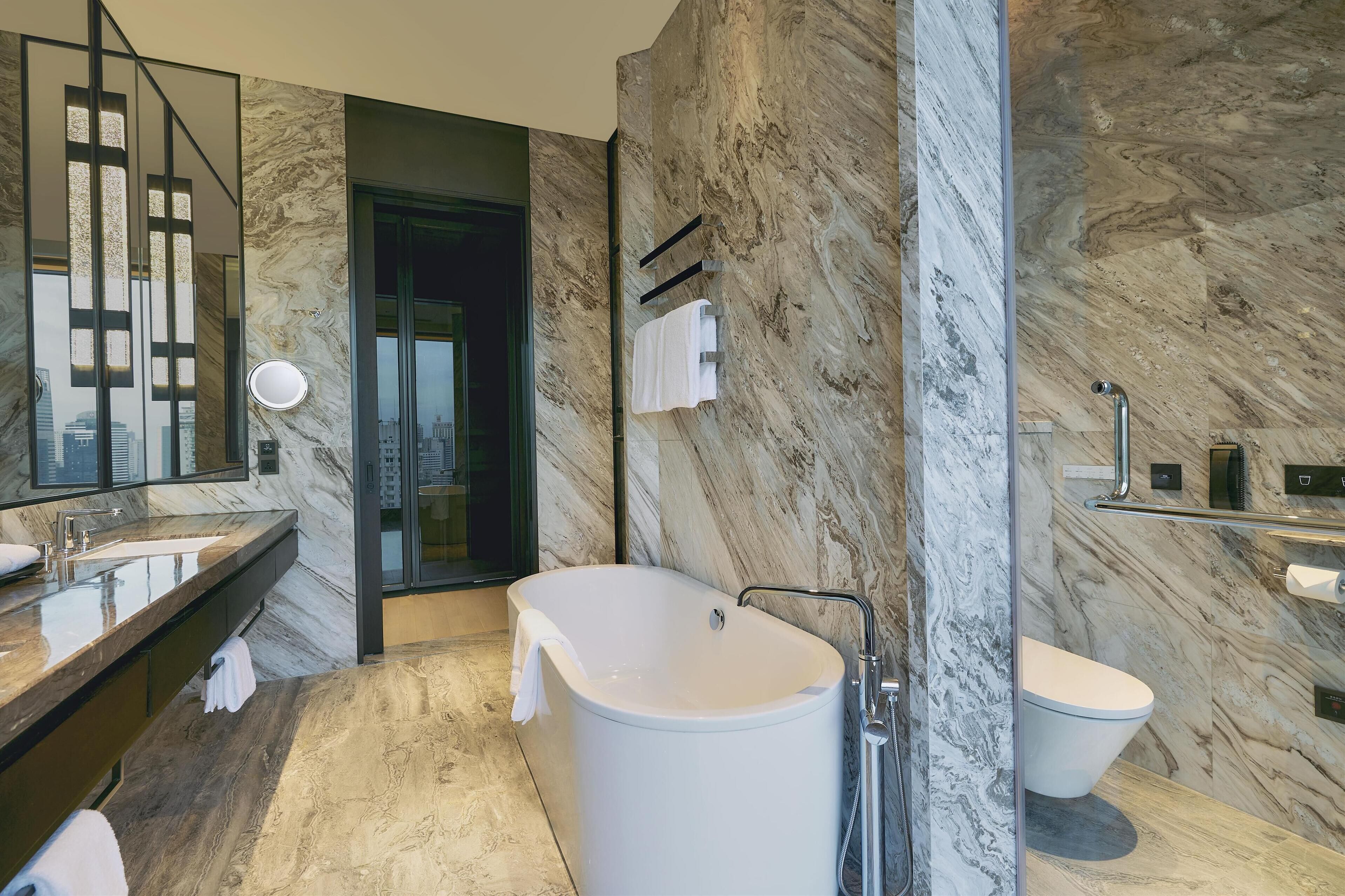 Un baño moderno con una bañera independiente, un espejo grande y paredes de mármol.