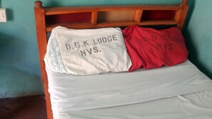 A bed with a wooden headboard and two pillows, one white and one red, with text on them. - Dgk Lodge (Naivasha)